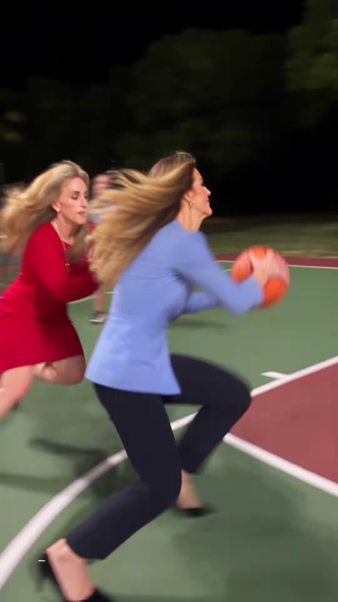 Credited source frame at about one second: the attacker in a light-blue blazer and black trousers drives with the ball past the defender in red on a green and maroon outdoor court at night