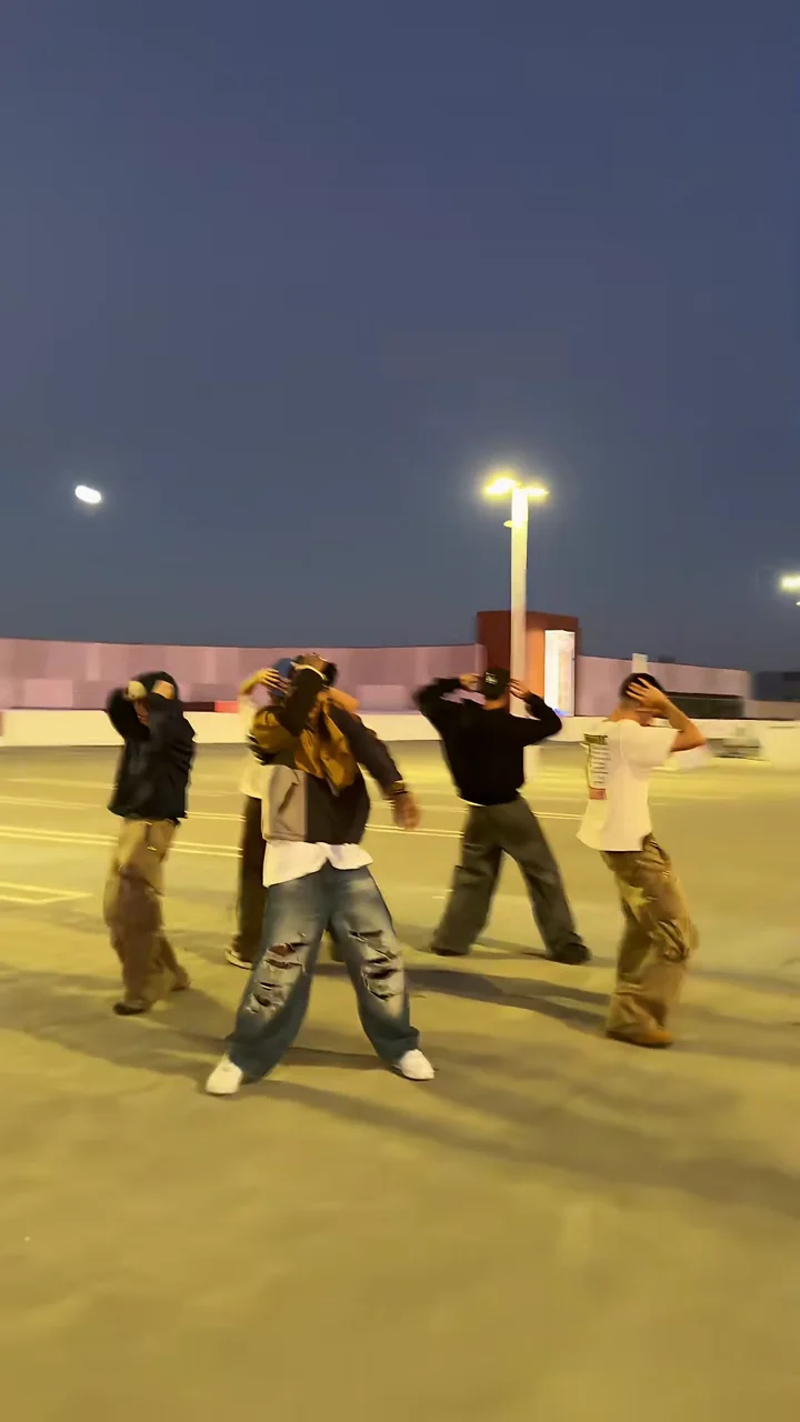 Credited source frame at about 15.5 seconds: the crew stands with both hands on their heads on the rooftop at dusk under a light pole