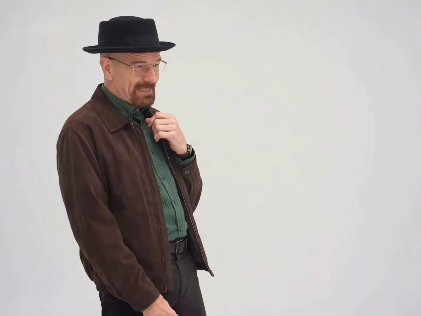 Credited source reel frame at about four seconds: a man in a black pork-pie hat and brown jacket stands against a plain light-grey backdrop with one hand raised to his chest