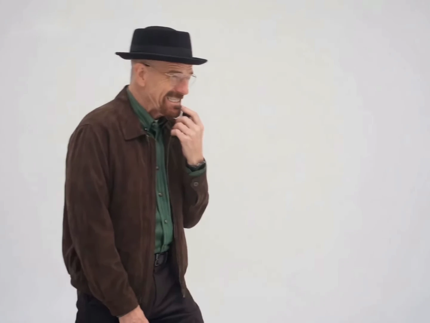 Credited source reel frame at about seven and a half seconds: a man in a black pork-pie hat and brown jacket raises a hand to his mouth against a plain grey backdrop